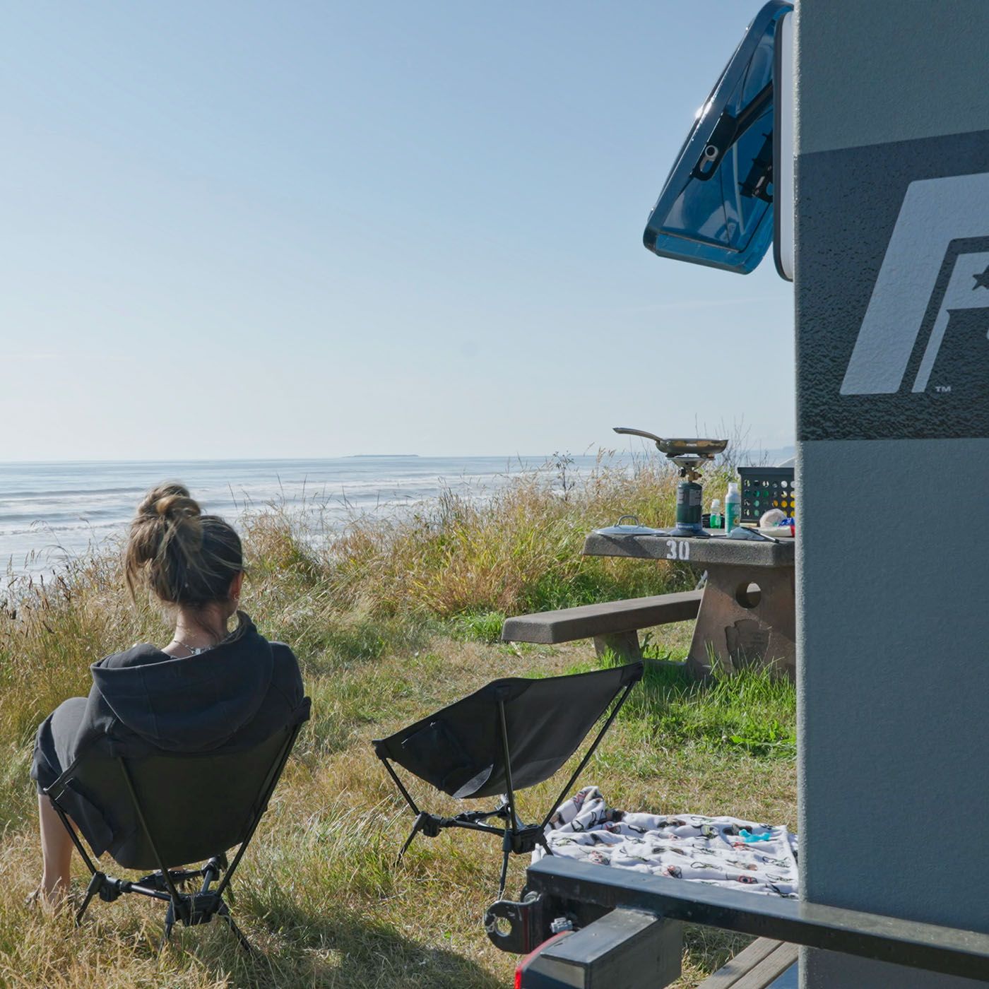 Woman looking at ocean sitting outside her trailer camper by Freedom Campers