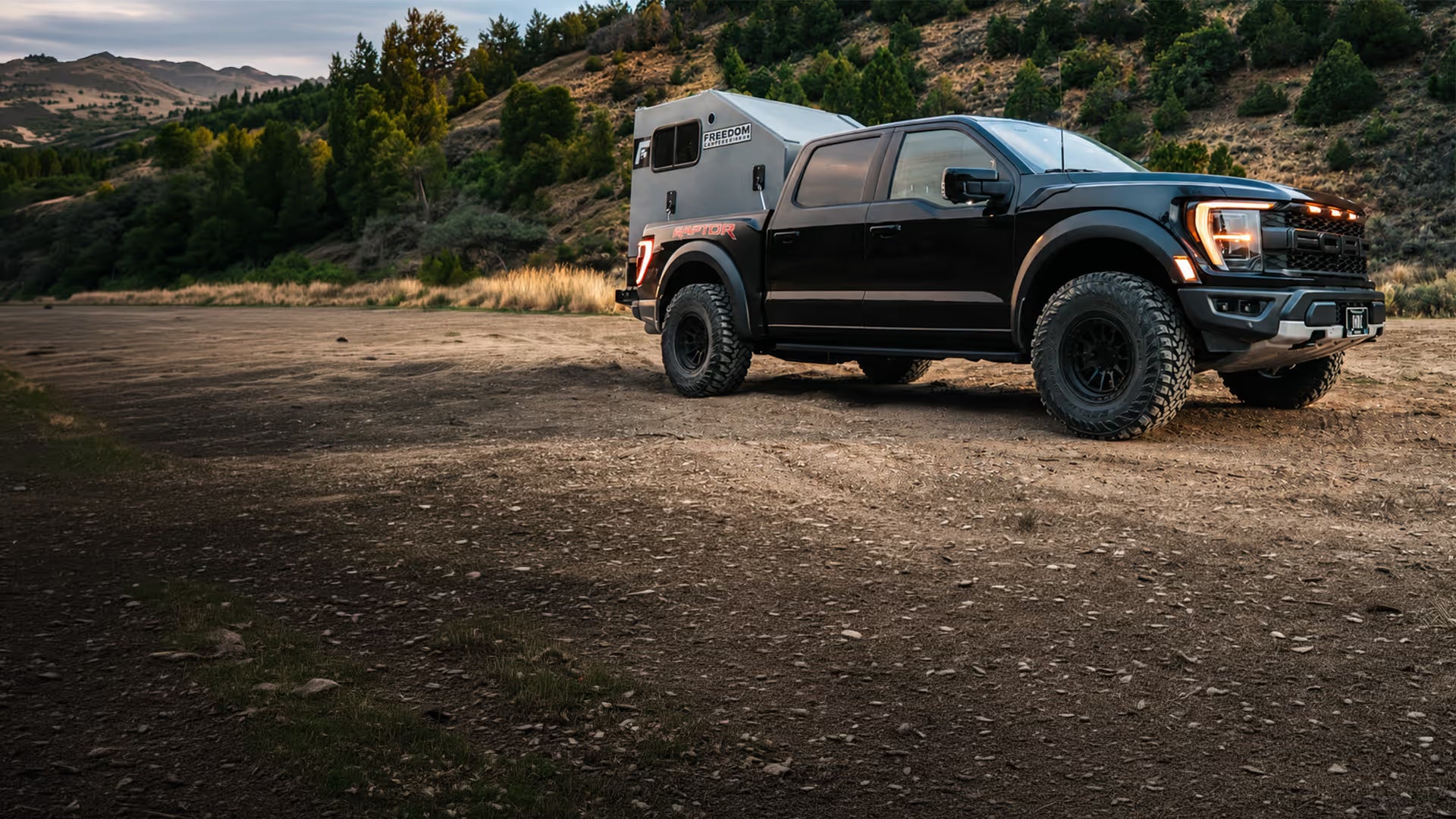 Freedom Camper in the back of a Ford Raptor driving on a dirt path in the mountains.